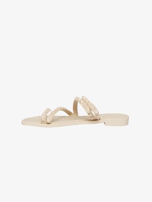 Sandali modellati beige con due cinturini testurizzati e dettagli a piramide, suola piatta e design minimalista. Adatti per un abbigliamento casual.