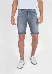 Lichtblauwe denim shorts met een vervaagde afwerking, voorzien van omgerolde pijpen en een klassieke vijf-pocket stijl, gedragen met witte sneakers.