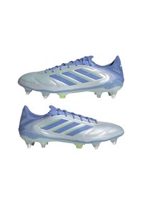 Crampons de football bleu clair avec trois rayures bleu foncé, surface texturée, conception à lacets, et pointes translucides sur une semelle dégradée.