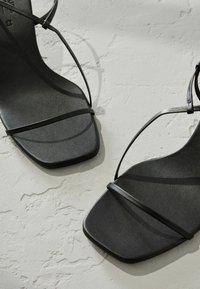 Schwarze Riemchensandalen mit quadratischer Zehenpartie, aus glattem Leder gefertigt, mit dünnen Riemen und einer flachen Sohle mit dezenter Textur.