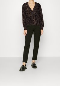Halenka s potiskem leopardí kůže v tmavých tónech, s dlouhými rukávy a výstřihem do V, spárovaná s slim-fit černými kalhotami a masivními černými mokasíny.