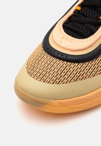 Sneaker con una parte superiore in rete nera e arancione testurizzata, suola beige chiaro e un design curvo con una prominente punta in gomma.