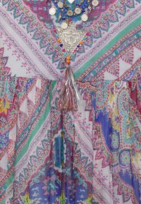 Robe à motifs multicolores présentant des dessins floraux et géométriques complexes, ornée d'un pendentif triangulaire argenté et de perles multicolores au niveau du col.