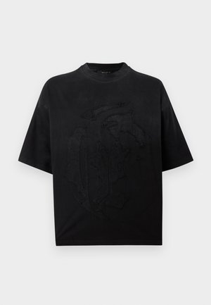 Czarny oversize t-shirt z krótkim rękawem i okrągłym dekoltem z dużym naszytym abstrakcyjnym wzorem z przodu na jednolitym białym tle.