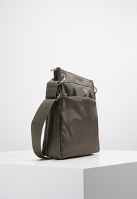 Olivově zelená kabelka přes rameno z odolné látky, vybavená zapínáním na zip, nastavitelným popruhem a texturovanými stranami s kontrastním prošitím.