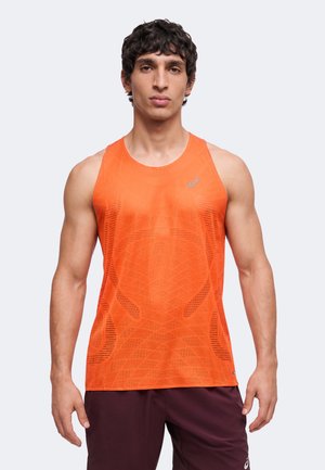 Jeune homme portant un débardeur de sport orange vif et un short foncé, debout devant un fond clair uni.