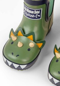 Botas de lluvia de goma verdes con diseño de cara de dinosaurio. Cuenta con acentos amarillos y negros, picos tridimensionales y un patrón de dientes en zigzag en la puntera.