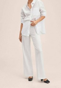 Chemise blanche à boutons avec une poche, associée à un pantalon blanc large ajusté et des chaussures noires à bout carré. Tissu lisse avec une coupe décontractée.