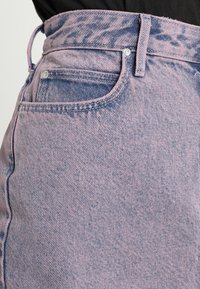 Jean en denim rose clair taille haute avec une finition texturée, doté d'un design classique à cinq poches et d'une fermeture à bouton métallique.