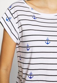 Vit T-shirt med svart horisontella ränder och liten blå ankarebroderi. Mjuk bomullstyg, avslappnad passform och bred båturringning.