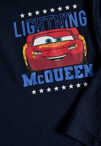 Marinblå t-shirt med en färgglad grafik av Blixten McQueen, med vit och blå text samt stjärnaccenter ovanför och nedanför bilden.