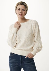 Crème-kleurige gebreide trui met een gestructureerd ruitpatroon en geribbelde manchetten, gecombineerd met donkerblauwe jeans. Zachte, relaxte pasvorm.
