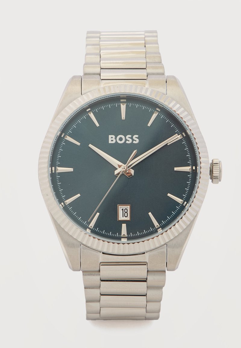 Αναλογικό ρολόι χειρός από ασημί μέταλλο με μαύρο καντράν, ασημί δείκτες ώρας, το λογότυπο "BOSS" και ένδειξη ημερομηνίας που δείχνει 18, σε μπρασελέ από μεταλλικούς συνδέσμους.