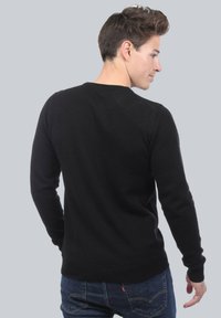 Pull en maille noire avec des manches longues et un col rond, présentant une texture lisse et un design ajusté, vu de dos.