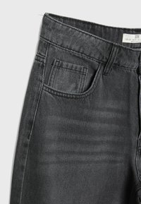 Acercamiento a unos pantalones vaqueros de mezclilla gris oscuro que muestra el bolsillo frontal, el pequeño bolsillo para monedas, los pasantes de cinturón y los detalles de costura de la cinturilla.
