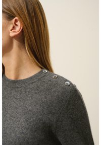 Szary wełniany sweter z okrągłym dekoltem i trzema dekoracyjnymi guzikami na ramieniu. Miękka faktura i dopasowany krój.