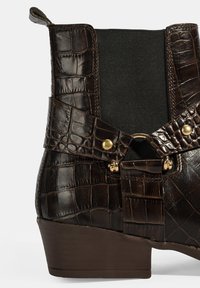 Botte de cheville en cuir d'alligator brun avec une surface texturée, un panneau latéral élastique, un accent en matériel doré et un talon effilé.