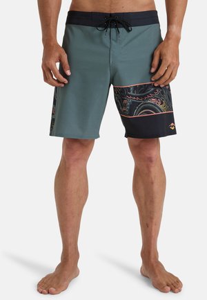 Shorts de bain pour homme en bleu canard et noir. Présentent un design texturé avec un motif de vagues, une taille élastique avec cordon de serrage ajustable et un matériau léger.