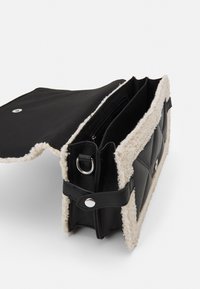 Svart läderväska med fårskinnsdetaljer, med lockstängning, flera fack och tryckknapp. Texturerad yta.