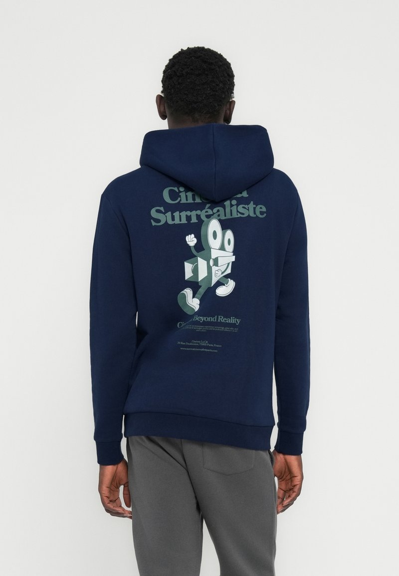 Μπλε σκούρο φούτερ με κουκούλα, με γραφικό σχέδιο που απεικονίζει ένα καρτούν χαρακτήρα και κείμενο σε πράσινο, με ριμπ μανσέτες και στρίφωμα. Το ύφασμα φαίνεται μαλακό.