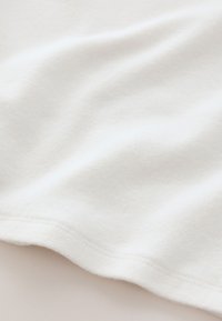 White soft fabric with a smooth texture, showing gentle folds and seams, ideal for clothing or textiles. Lightweight and minimally textured.