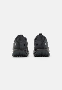 Zwarte sportieve schoenen met een gestructureerde mesh bovenkant, ronde hak, reflecterende accenten en een robuuste rubberen buitenzool voor grip.