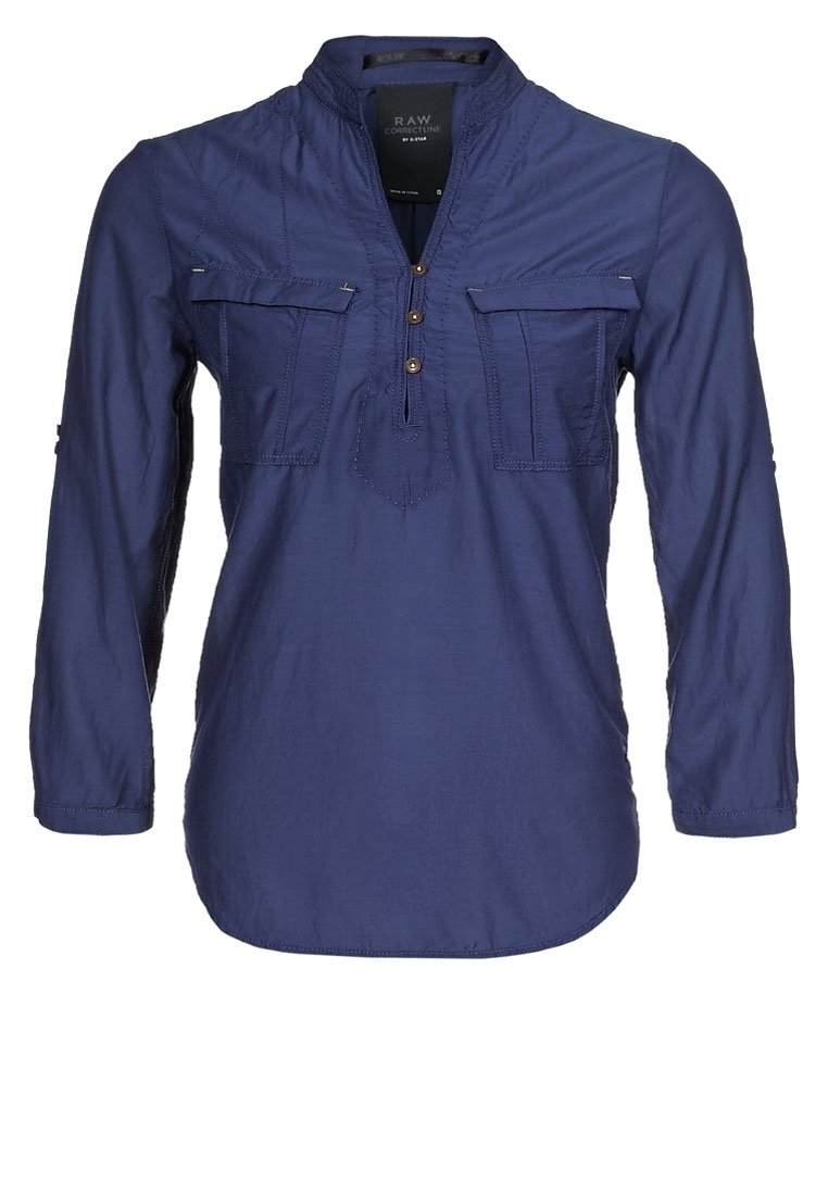 Chemise à manches longues bleu marine avec un col, deux poches avant, trois boutons marron et des détails de couture subtils. Tissu léger, coupe décontractée.