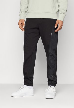 Zwarte joggers met een getextureerd zijpaneel, elastische manchetten en een zak met rits. Gecombineerd met witte lage sneakers en een lichtgroene sweatshirt.