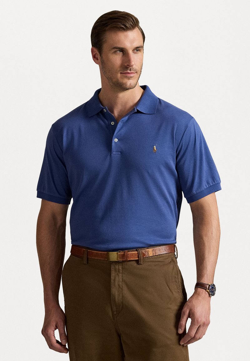 Cămașă polo albastră cu mâneci scurte, guler clasic și un mic logo pe piept; asociată cu pantaloni maro și o curea din piele.