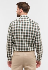 Geruite shirt in groen, bruin en wit, met lange mouwen, een button-down kraag en een rechte achterkant. Een paar beige broeken zichtbaar.