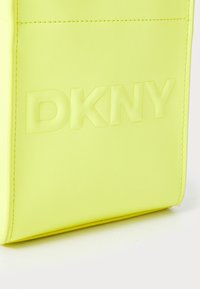 Neon rumena DKNY torba, izdelana iz gladkega sintetičnega materiala, s poudarjenim logotipom in čistim šivom v pravokotni zasnovi.