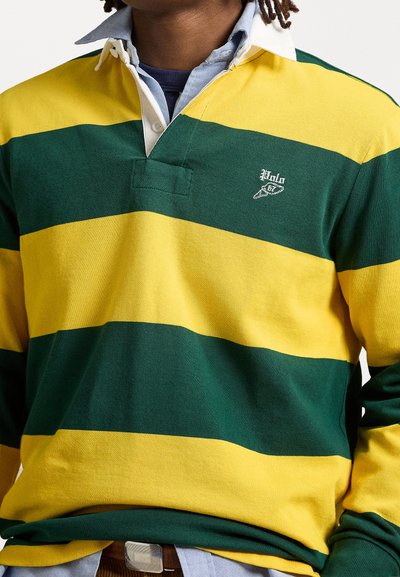 Groen-gele gestreepte rugbyshirt met lange mouwen, een witte kraag en een geborduurd logo. De stof lijkt van katoen te zijn, met een zachte textuur.