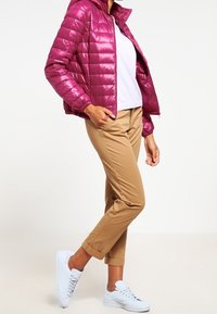 Lekki, błyszczący magenta puchowy jackiet z zamekiem z przodu, w zestawieniu z beżowymi chinosami i białymi trampkami. Gładka tekstura, luźny krój.