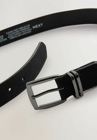 Cinturón de cuero negro con un acabado mate, que cuenta con una hebilla rectangular plateada y tres acentos de metal negro cerca de la hebilla.