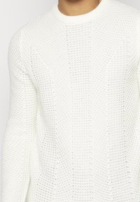 Witte gebreide trui met een gestructureerde weefpatroon, ribbels aan de halslijn en lange mouwen, met een losse pasvorm en een open steekpatroon.