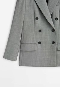 Blazer grigio doppiopetto con grandi bottoni neri, spalle strutturate e un tessuto testurizzato. Presenta due tasche frontali e una vestibilità su misura.