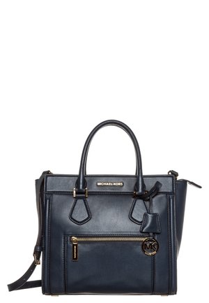 Czarna skórzana torebka Michael Kors z górnymi uchwytami, przednią kieszenią na zamek błyskawiczny oraz złotym zawieszką z logo MK, na białym tle.