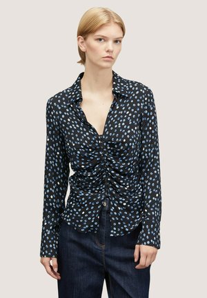 Zwarte longsleeve shirt met lichtblauwe ovale patronen, gerimpelde details aan de voorkant en een kraaghalslijn. Gecombineerd met donkere denim.