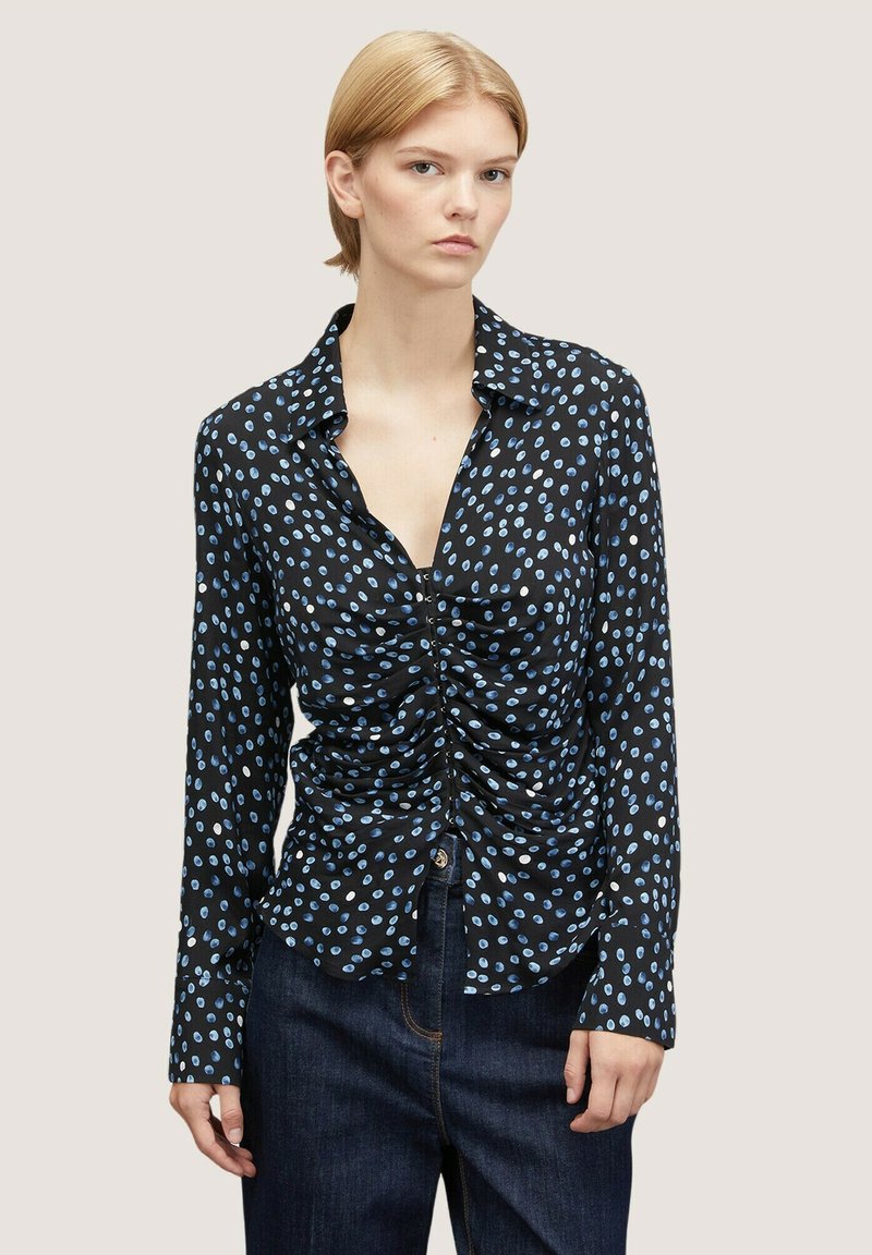Černá dlouhá rukávová košile s světle modrými oválnými vzory, na přední straně s nařasením a s límečkem. Spárováno s tmavými džíny.