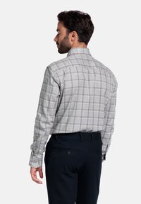 Grijs geruit overhemd met blauwe en rode accenten, voorzien van een button-down kraag en lange mouwen. Gecombineerd met donkerblauwe broeken.