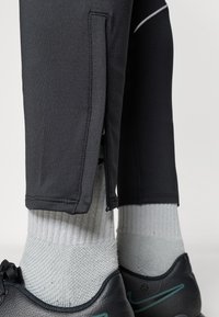 Μαύρο αθλητικό παντελόνι με φερμουάρ στις πλαϊνές ραφές, συνδυασμένο με γκρι ριγέ κάλτσες και μαύρα παπούτσια με τουρκουάζ λεπτομέρειες.