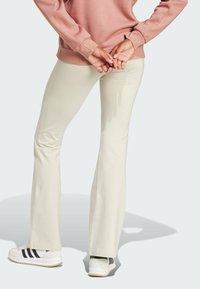 Svetlo bež razširjene hlače iz raztegljive tkanine. Imajo gladko teksturo in so v kombinaciji z belimi športnimi čevlji z črnimi črtami.