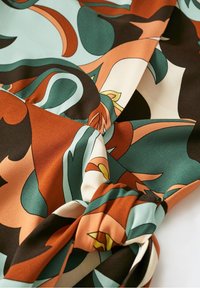 Tissu doux avec un motif floral abstrait en bleu sarcelle, rouille, crème et noir, présentant un détail de couture froncée sur une section.