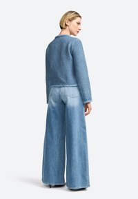 Giacca lavorata a maglia azzurro chiaro con colletto rotondo, abbinata a pantaloni in denim azzurro chiaro a gamba larga, dotati di tasche posteriori e tessuto morbido.