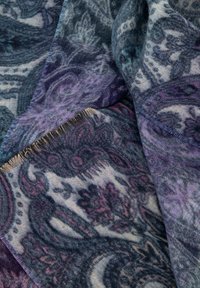 Un tessuto a fantasia in tonalità di blu, viola e crema, con design intricati e bordi frangiati per texture.