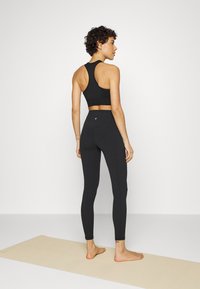Fekete sportos cropped felső és magas derekú leggings, rugalmas anyagból. Sportos kialakítású, racerback stílusú, karcsúsított fazonnal, amelyhez egy jóga szőnyeg tartozik.