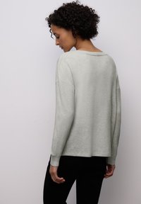 Světlé šedé pulovrové svetr s volnějším střihem, žebrovanými manžetami a kulatým výstřihem, vyrobený z měkké texturované látky.