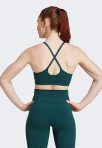 Sujeción deportiva verde con tirantes cruzados en la espalda, combinada con leggings de cintura alta. Ambos están confeccionados con un material suave y elástico con un mínimo de marcas.