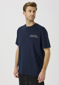 Granatowy bawełniany t-shirt z krótkimi rękawami, z białym nadrukiem na przodzie z napisem "Porte d'Auteuil" i współrzędnymi. Prosty design, luźny krój.