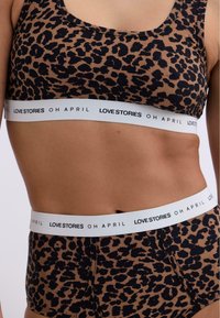 Leopardmønstret bralette og høj talje trusser i brun og sort, med et hvidt elastisk bånd med teksten "LOVE STORIES OH APRIL".